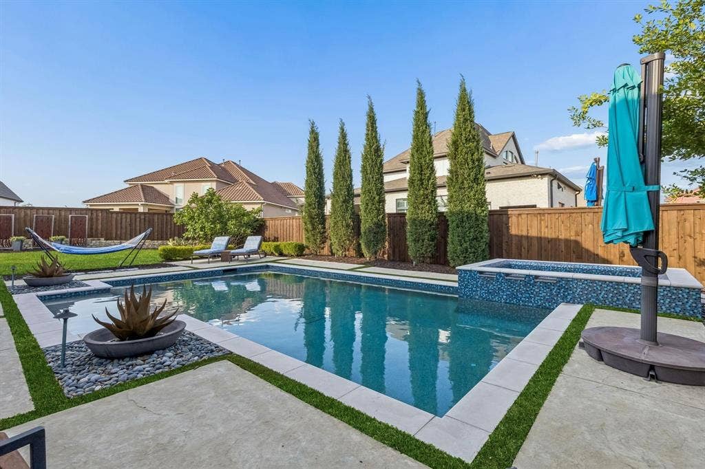 7342 Shoestring Drive, Frisco, TX 75036 Backyard featuring a rectangular swimming pool with integrated spa, concrete hardscaping with artificial turf accents, and mature trees providing privacy