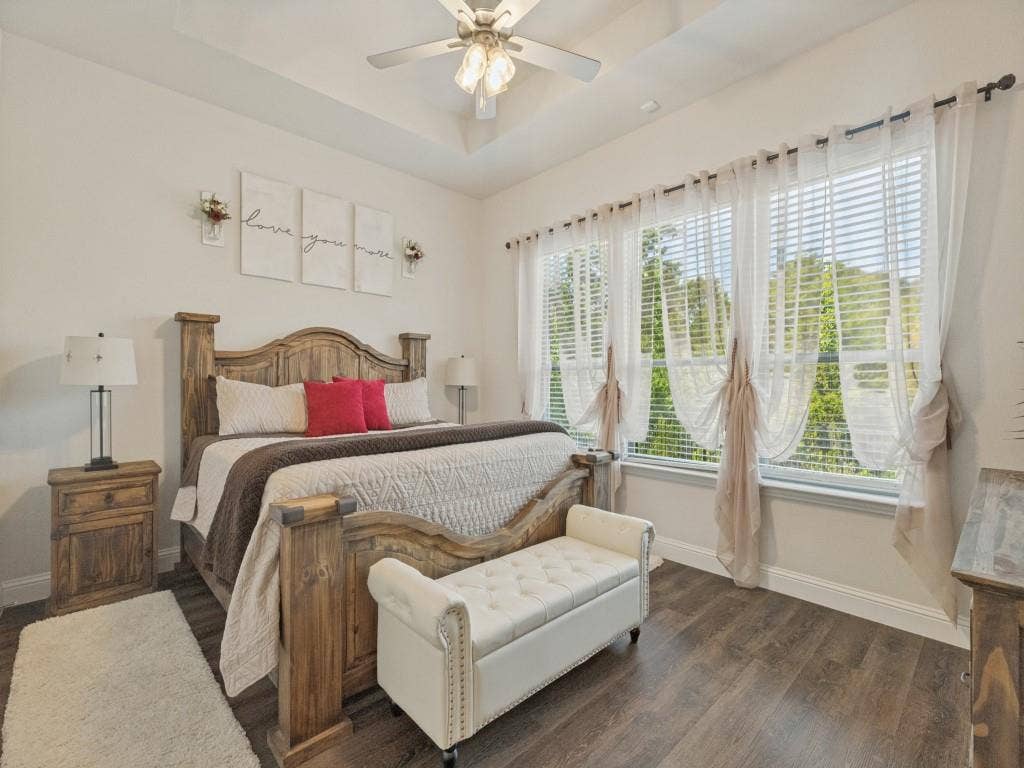 Tray ceiling with a ceiling fan, multiple large windows, and wood-finish flooring