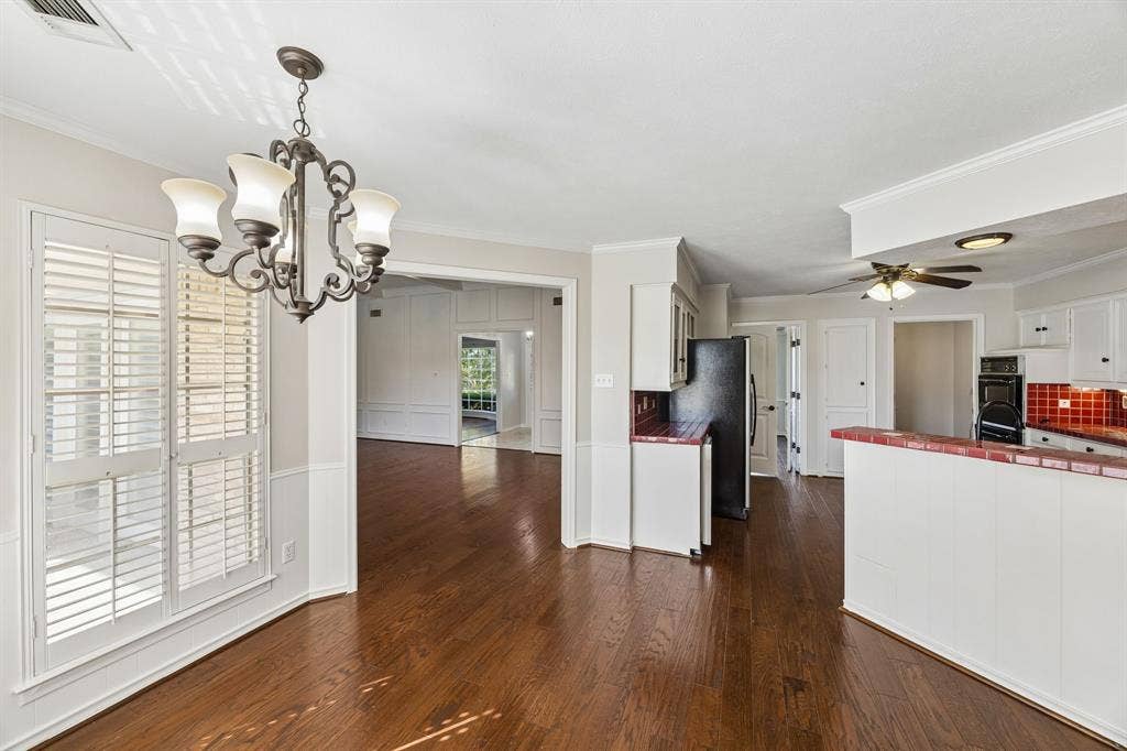 10322 White Rock Place, Dallas, TX 75238 Wood-finish flooring throughout, with a decorative chandelier, white plantation shutters, and a kitchen featuring red tile accents