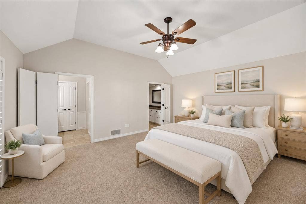 10322 White Rock Place, Dallas, TX 75238 Spacious primary bedroom featuring vaulted ceilings, neutral wall finishes, and new carpet. Ensuite bath with separate vanities and separate closets. This photo is virtually staged.