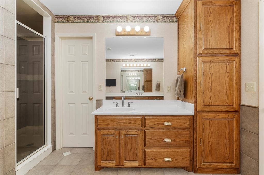 2029 Speegleville Road, Woodway, TX 76712 Bathroom featuring a glass-enclosed shower, wood-finish vanity with built-in storage, white countertop, and large wall-mounted mirror