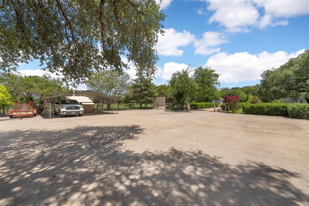 2029 Speegleville Road, Woodway, TX 76712 Expansive concrete parking area with a multi-vehicle carport and surrounding mature trees providing natural shade