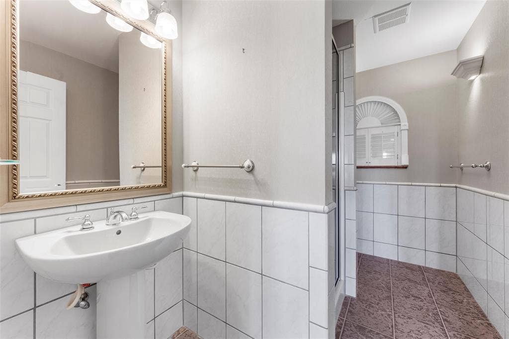 2029 Speegleville Road, Woodway, TX 76712 Pedestal sink with chrome fixtures, framed mirror, wall-mounted light fixture, and white tiled wainscoting