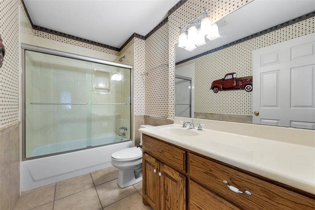 2029 Speegleville Road, Woodway, TX 76712 Tub and shower combination with sliding glass doors, single vanity with integrated sink, wood-finish cabinetry, and tiled flooring
