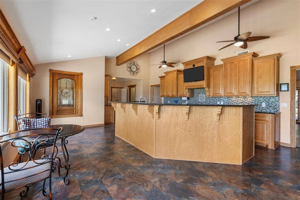 2029 Speegleville Road, Woodway, TX 76712 Vaulted ceilings, exposed wood beams, wood-finish cabinetry, patterned backsplash, and a breakfast bar