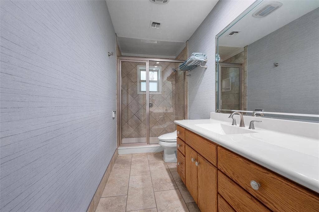 2029 Speegleville Road, Woodway, TX 76712 Double vanity with integrated sinks and brushed nickel faucets, wood-finish cabinetry, frameless mirror, tiled flooring, and a glass-enclosed shower with tiled surround