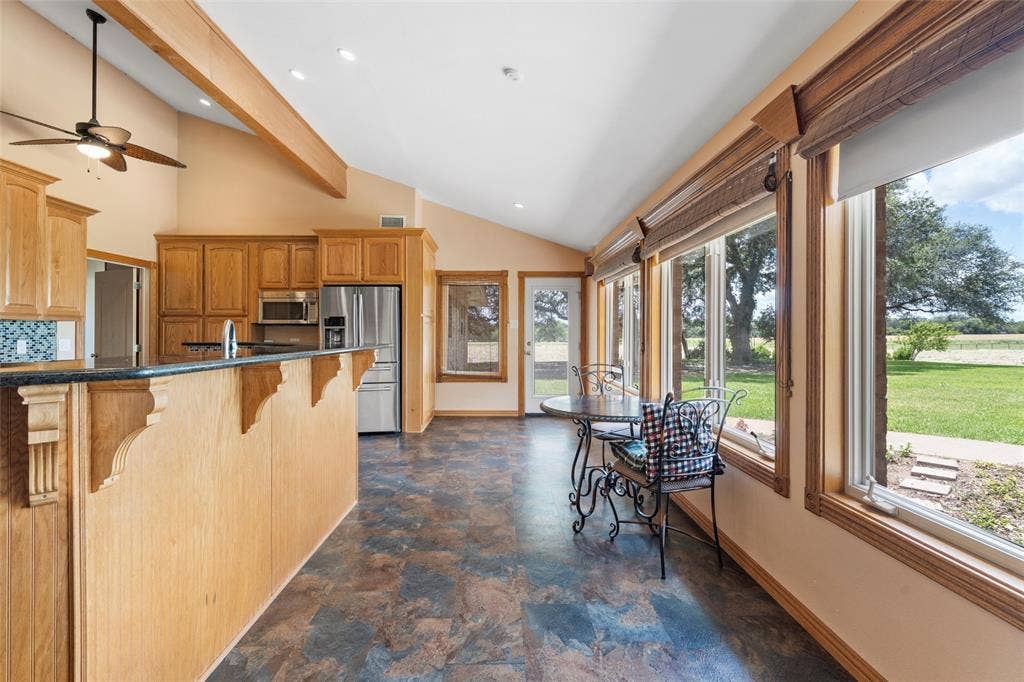 2029 Speegleville Road, Woodway, TX 76712 Vaulted ceiling with exposed wood beams, wood cabinetry, stainless steel appliances, large windows with roller shades, and a glass-paneled door