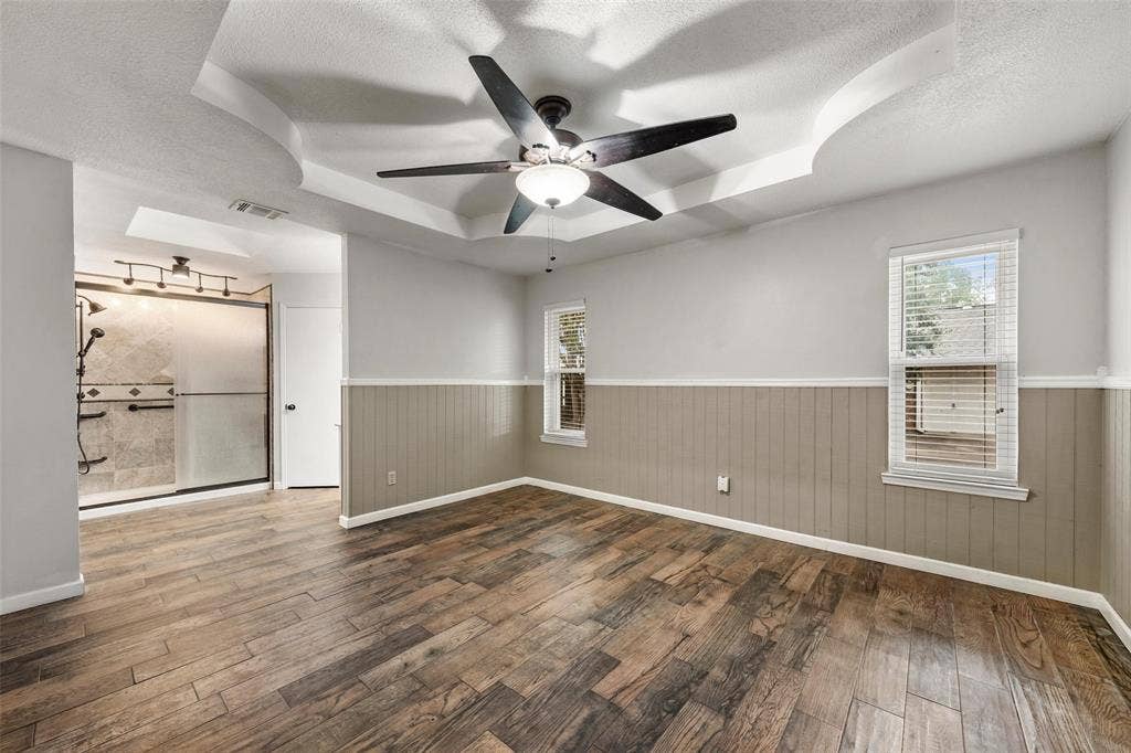812 Regina Drive, Hewitt, TX 76643 Tray ceiling with a ceiling fan, wood-finish flooring, two windows with blinds, wainscoting, and an adjacent shower with a glass enclosure