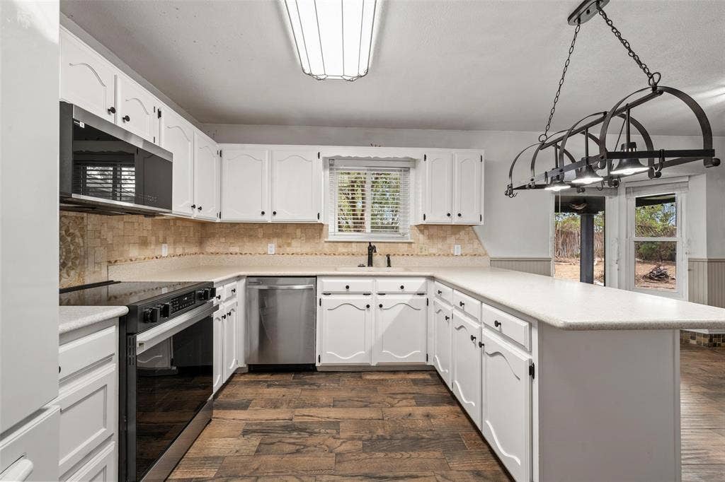 812 Regina Drive, Hewitt, TX 76643 White cabinetry with black hardware, stainless steel appliances, wood-finish flooring, light-toned countertops, and a modern linear chandelier