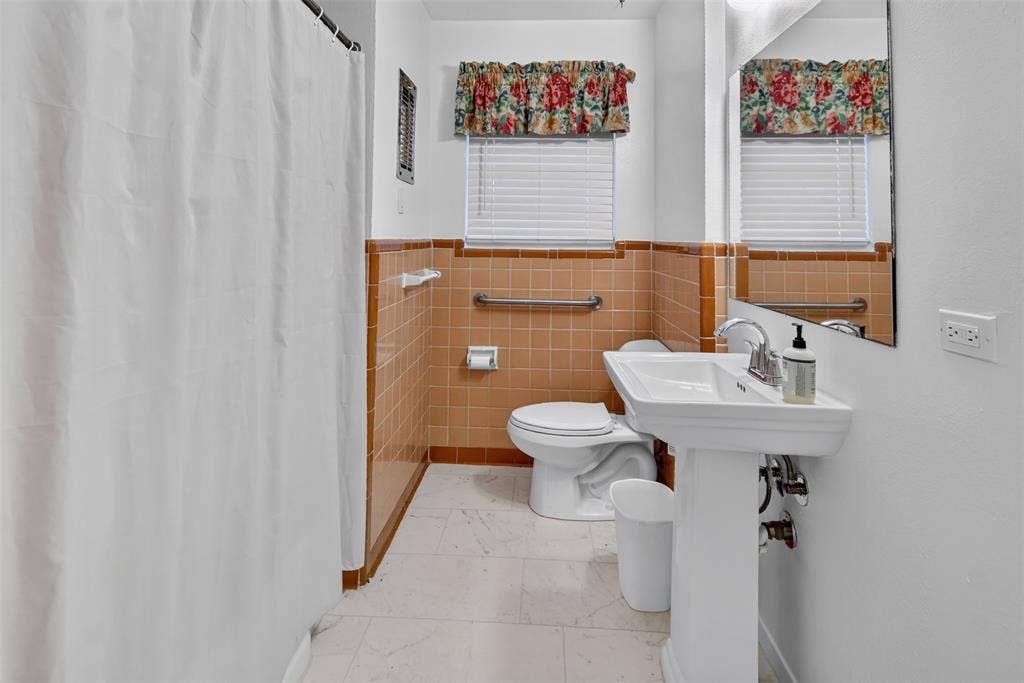 2024 Blake Avenue, Dallas, TX 75228 Pedestal sink with chrome faucet, wall-mounted mirror, tiled walls, and window with blinds