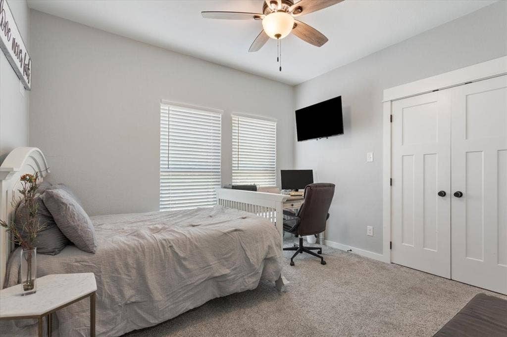 10305 Creekside Lane, Waco, TX 76712 Ceiling fan with integrated lighting, dual windows with blinds, built-in closet with panel doors and dark hardware, wall-mounted television, and carpeted flooring