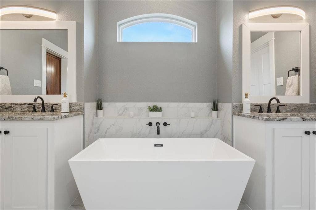10305 Creekside Lane, Waco, TX 76712 Freestanding soaking tub with wall-mounted faucet, dual vanities with granite countertops, and an arched transom window