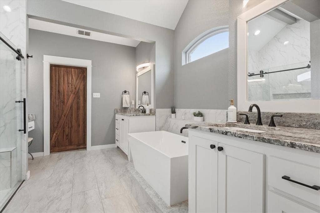 10305 Creekside Lane, Waco, TX 76712 Vaulted ceiling, freestanding soaking tub, dual vanities with stone countertops, arched transom window, and a sliding glass shower enclosure