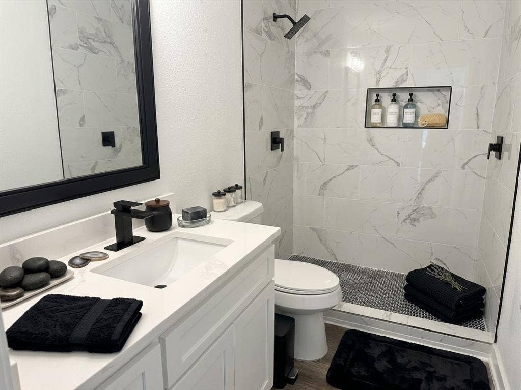 1424 E Parker Road, Plano, TX 75074 White vanity with integrated sink and matte black faucet, framed mirror, and tiled shower with built-in niche
