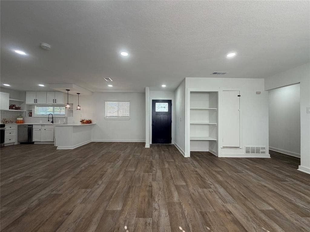 1424 E Parker Road, Plano, TX 75074 Open-concept living area featuring wood-finish flooring, recessed lighting, built-in shelving, a modern kitchen with white cabinetry, and a dark-paneled entry door with decorative glass