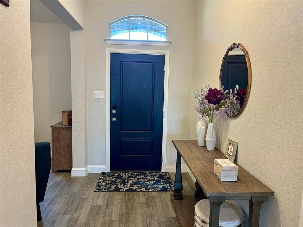 3636 Wintergreen Street, Grand Prairie, TX 76065 Entryway featuring a dark paneled door, an arched transom window, wood-finish flooring, and white baseboards