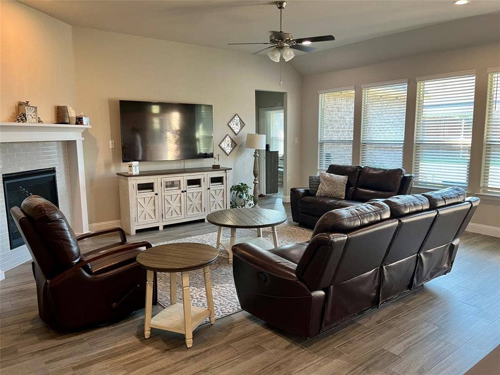 3636 Wintergreen Street, Grand Prairie, TX 76065 Vaulted ceiling with a ceiling fan, fireplace with a tile surround and mantel, wood-finish flooring, and multiple windows