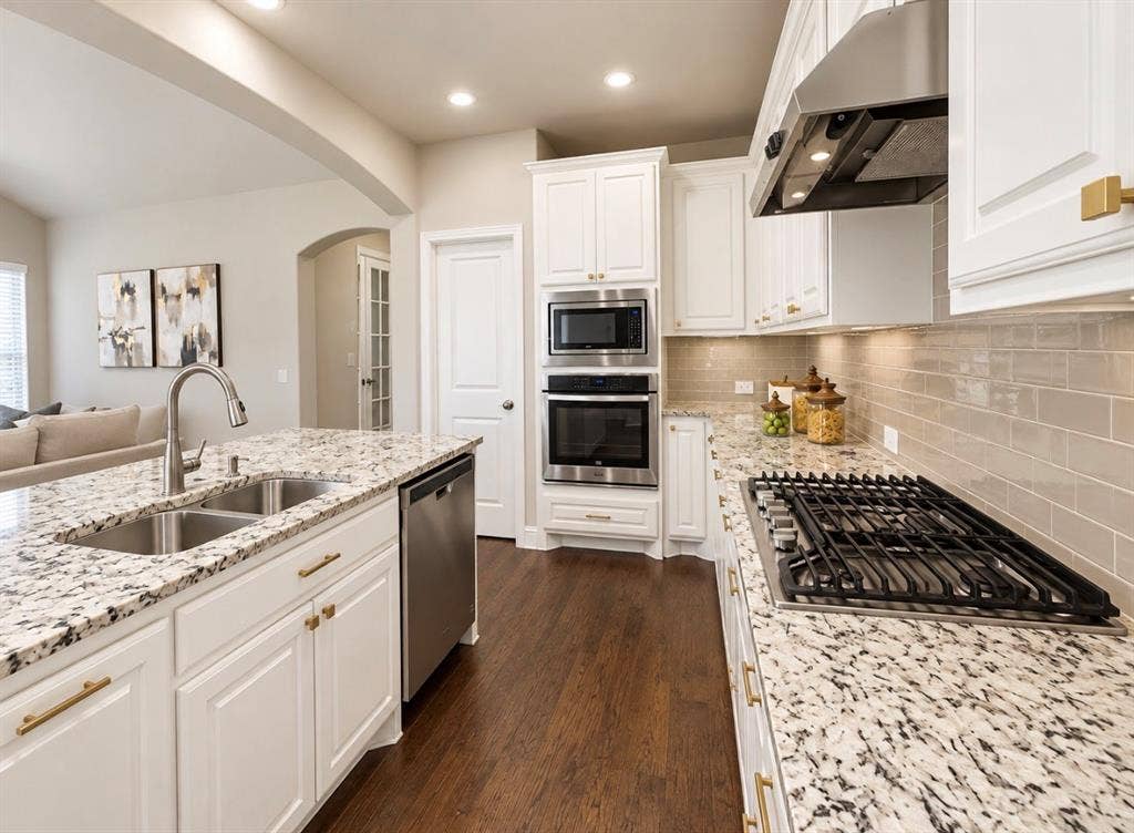 16116 Plum Court, Prosper, TX 75078 Kitchen featuring white cabinetry, built-in stainless steel appliances, a gas cooktop, light-toned subway tile backsplash, and speckled countertops