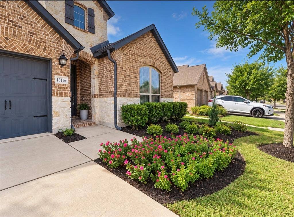 16116 Plum Court, Prosper, TX 75078 Brick and stone facade, dark gray garage door, arched entry, decorative shutters, and mature landscaping