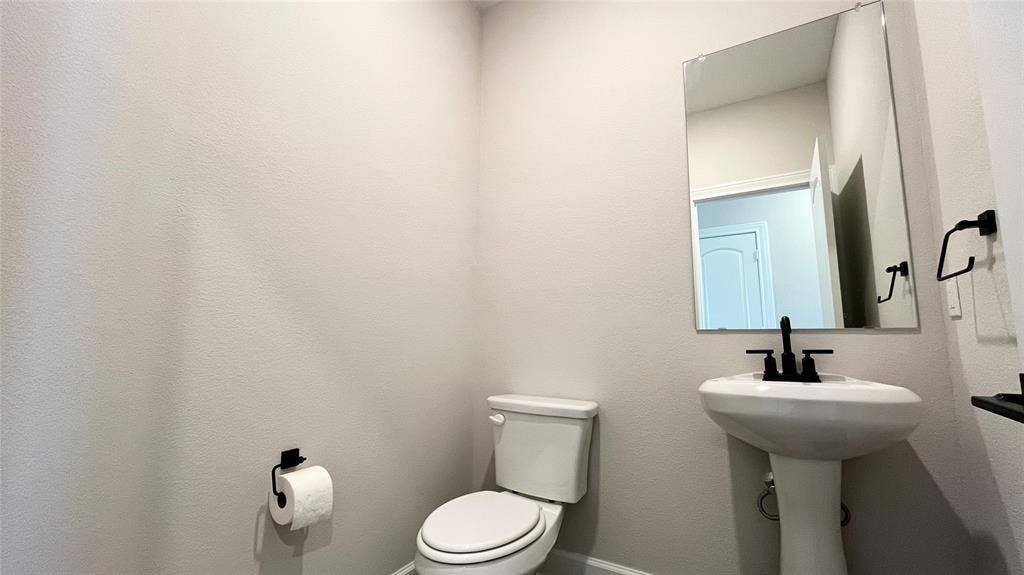 1101 Princeton Heights, Princeton, TX 75407 Pedestal sink with a matte black faucet, wall-mounted mirror, and white toilet
