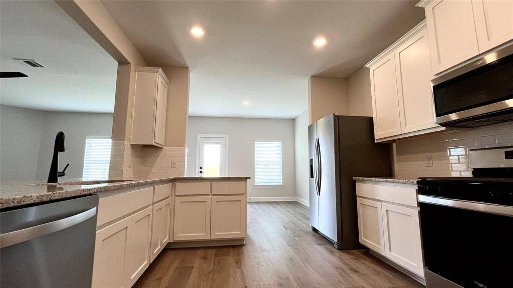 1101 Princeton Heights, Princeton, TX 75407 Kitchen featuring white shaker-style cabinetry, stainless steel appliances, granite countertops, and wood-finish flooring