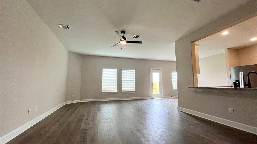 1101 Princeton Heights, Princeton, TX 75407 Spacious interior featuring wood-finish flooring, multiple windows, a ceiling fan, and a kitchen pass-through with a breakfast bar