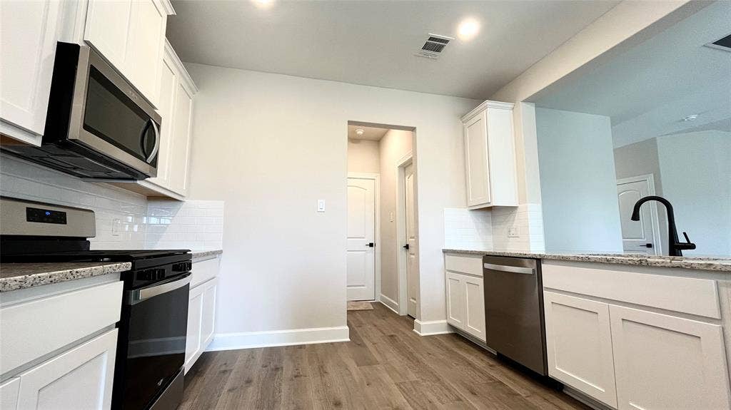 1101 Princeton Heights, Princeton, TX 75407 Kitchen featuring granite countertops, white cabinetry, stainless steel appliances, wood-finish flooring, and a subway tile backsplash