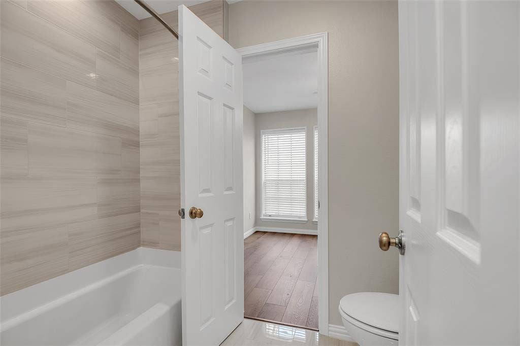 3635 Garden Brook Drive, #20200L, Farmers Branch, TX 75234 Bathroom featuring a white bathtub, light-toned tiled shower surround, and a white toilet