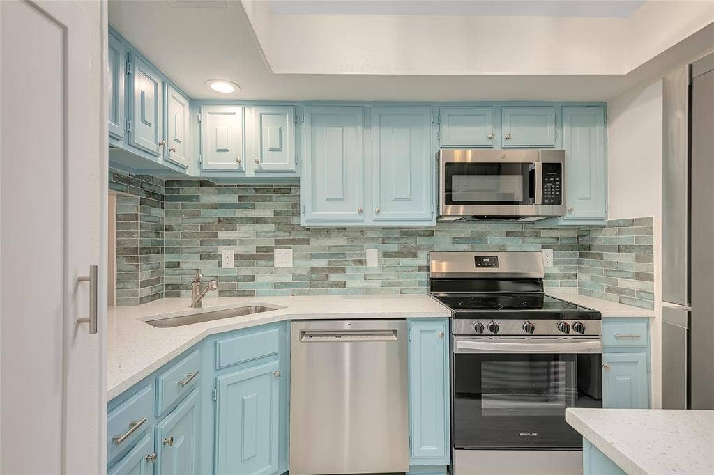 3635 Garden Brook Drive, #20200L, Farmers Branch, TX 75234 Kitchen featuring light blue cabinetry, stainless steel appliances, white countertops, and a full-height tile backsplash