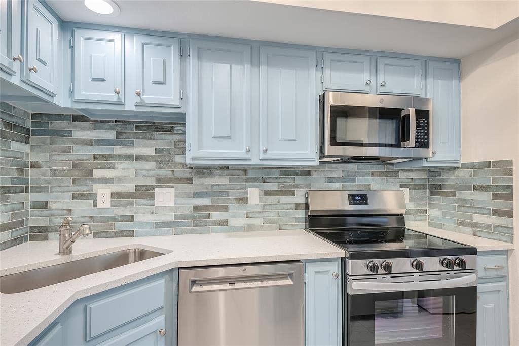 3635 Garden Brook Drive, #20200L, Farmers Branch, TX 75234 Kitchen featuring light blue cabinetry, stainless steel appliances, a tile backsplash, light-toned countertops, and a corner sink