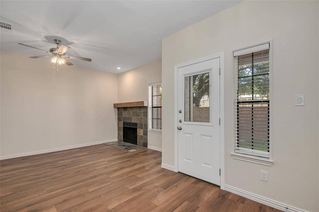 3635 Garden Brook Drive, #20200L, Farmers Branch, TX 75234 Wood-finish flooring, tiled fireplace with a wood mantle, ceiling fan, white paneled door with glass insert, and a window with blinds