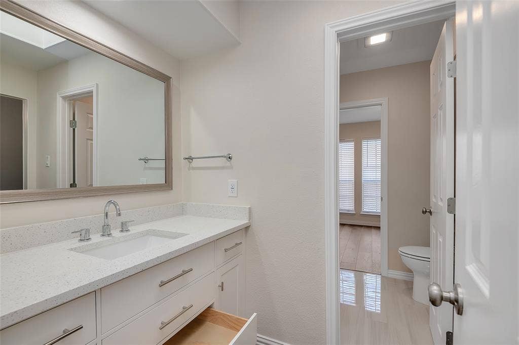 3635 Garden Brook Drive, #20200L, Farmers Branch, TX 75234 White vanity with ample storage, quartz countertop, chrome faucet, and rectangular framed mirror