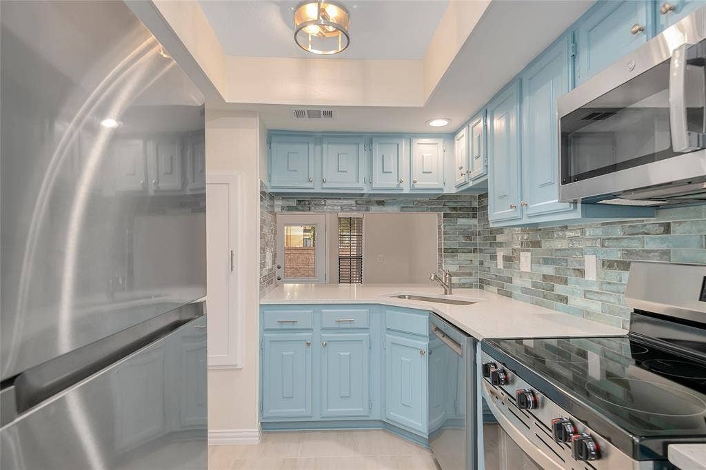 3635 Garden Brook Drive, #20200L, Farmers Branch, TX 75234 Light blue cabinetry with silver hardware, white countertops, glass tile backsplash, stainless steel appliances, and a recessed ceiling light fixture