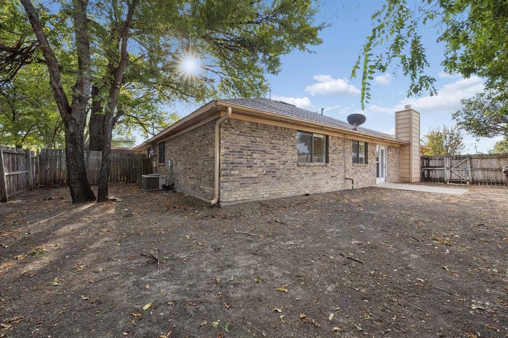 1613 19th Street, Plano, TX 75074 Brick exterior, multiple windows, a concrete patio, a wood fence, and mature trees
