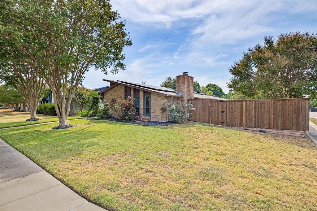 1216 Lombardy Drive, Plano, TX 75023 Brick exterior residence with a wood privacy fence, mature trees, and a concrete sidewalk