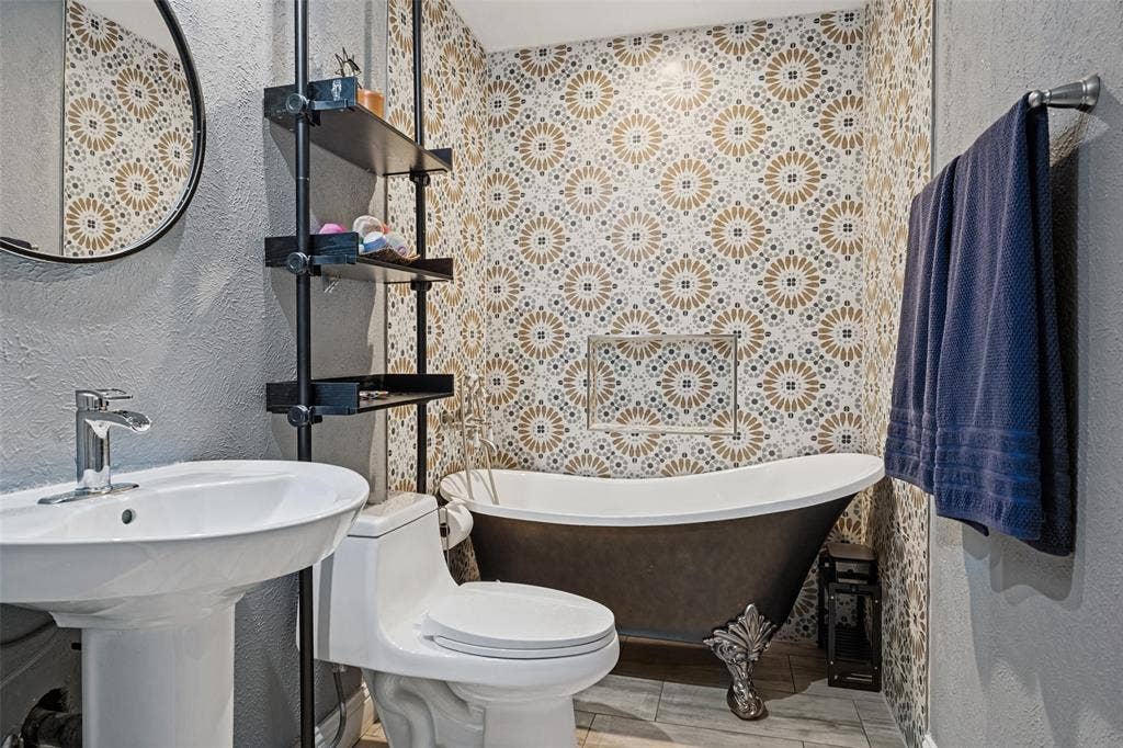 1216 Lombardy Drive, Plano, TX 75023 Pedestal sink with chrome faucet, floor-mounted toilet, freestanding clawfoot bathtub, patterned tile wall, and built-in shelving unit