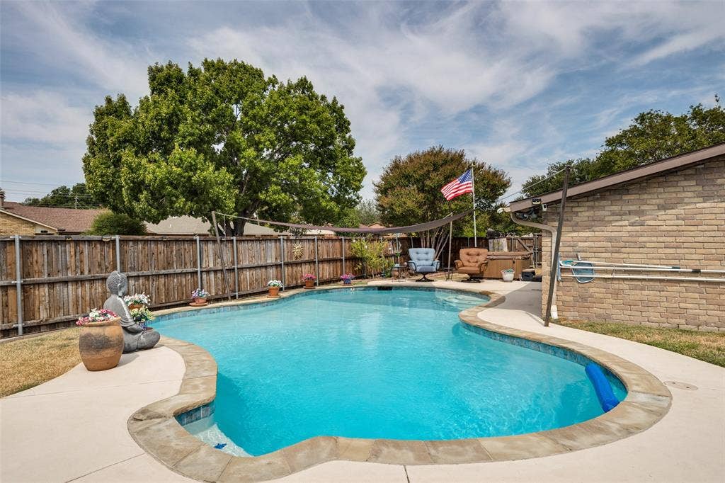 1216 Lombardy Drive, Plano, TX 75023 Freeform swimming pool with concrete decking, wood privacy fencing, and a brick-clad exterior