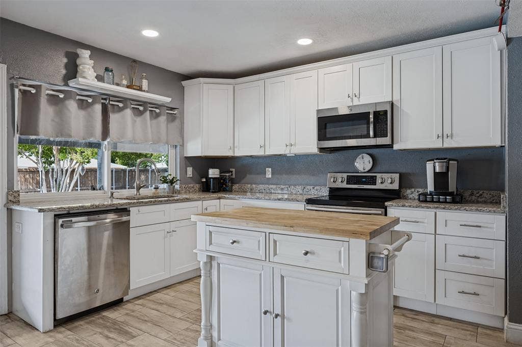 1216 Lombardy Drive, Plano, TX 75023 Kitchen featuring white shaker cabinetry, stainless steel appliances, granite countertops, wood-finish flooring, and a kitchen island with a butcher block top