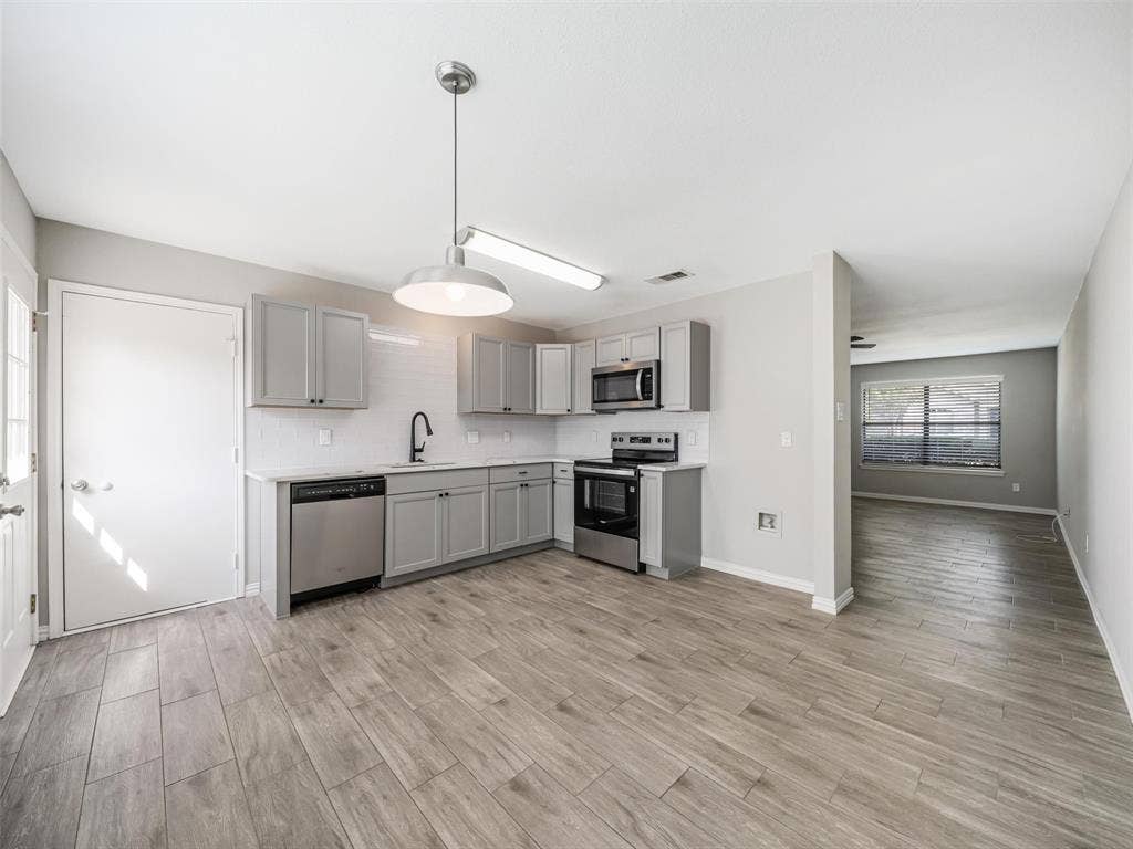 Modern kitchen featuring light gray cabinetry, stainless steel appliances, wood-finish flooring, and a white subway tile backsplash