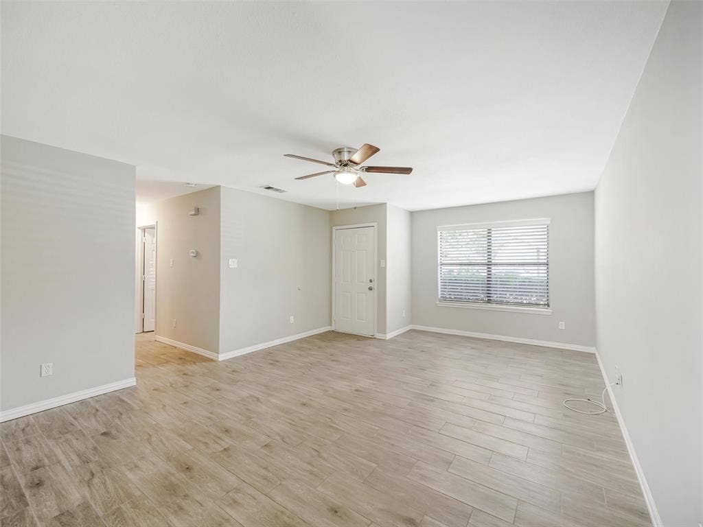 Spacious room featuring wood-finish flooring, a ceiling fan, and a large window with blinds