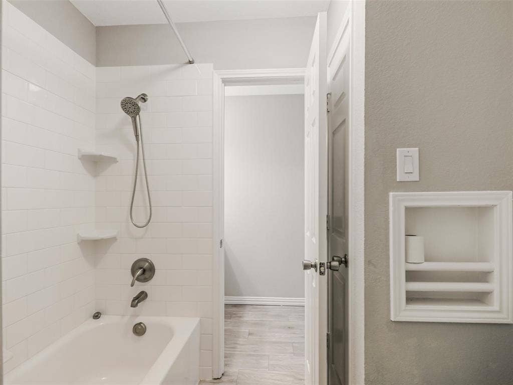 Bathtub with subway tile surround, brushed nickel fixtures, and integrated corner shelving
