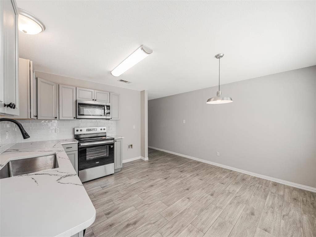 Kitchen featuring stainless steel appliances, light-toned cabinetry, subway tile backsplash, and wood-finish flooring
