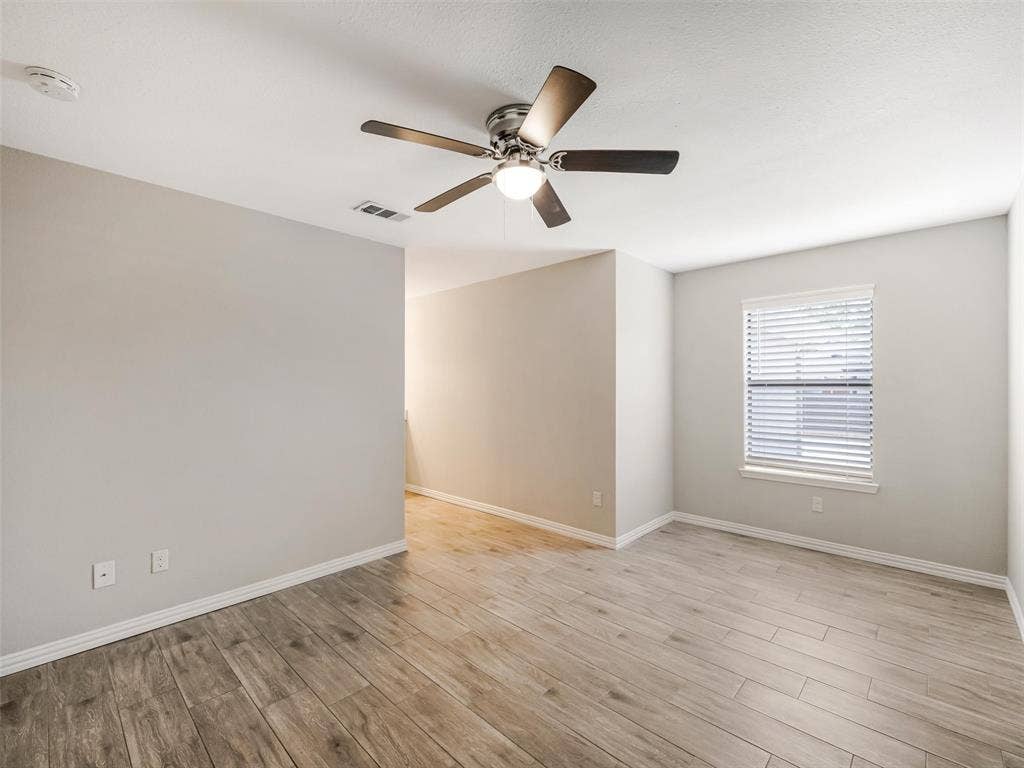 Wood-finish flooring, ceiling fan with integrated lighting, window with blinds, and light-toned wall finishes