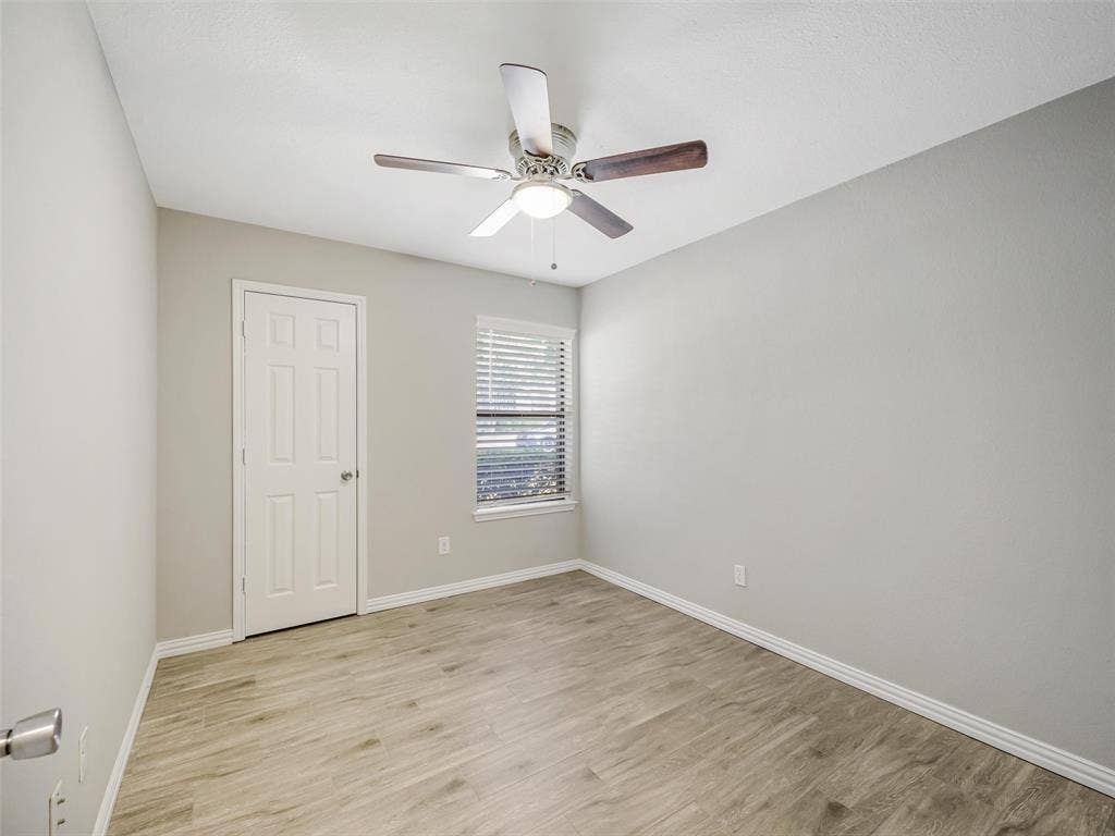 Wood-finish flooring, ceiling fan with integrated lighting, window with blinds, and a paneled door
