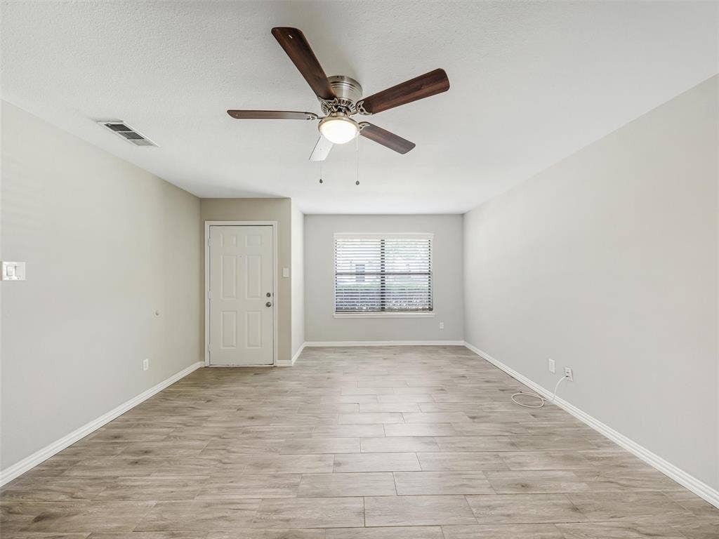 Spacious room featuring wood-finish flooring, a ceiling fan with integrated lighting, and neutral wall paint