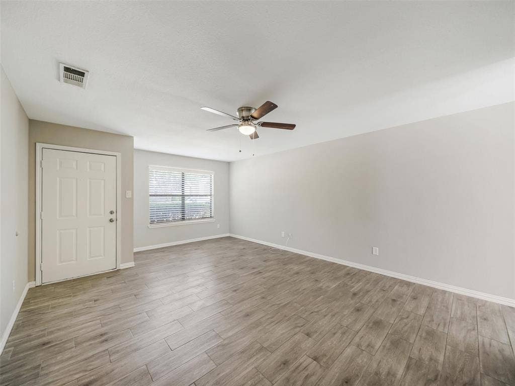 Neutral wall tones, wood-finish flooring, ceiling fan with integrated lighting, and window with blinds