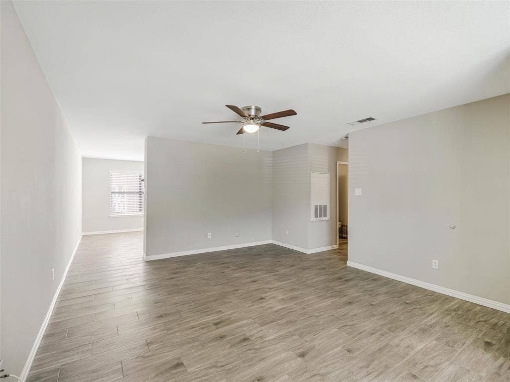 Spacious room featuring wood-look tile flooring, light-toned walls, and a ceiling fan