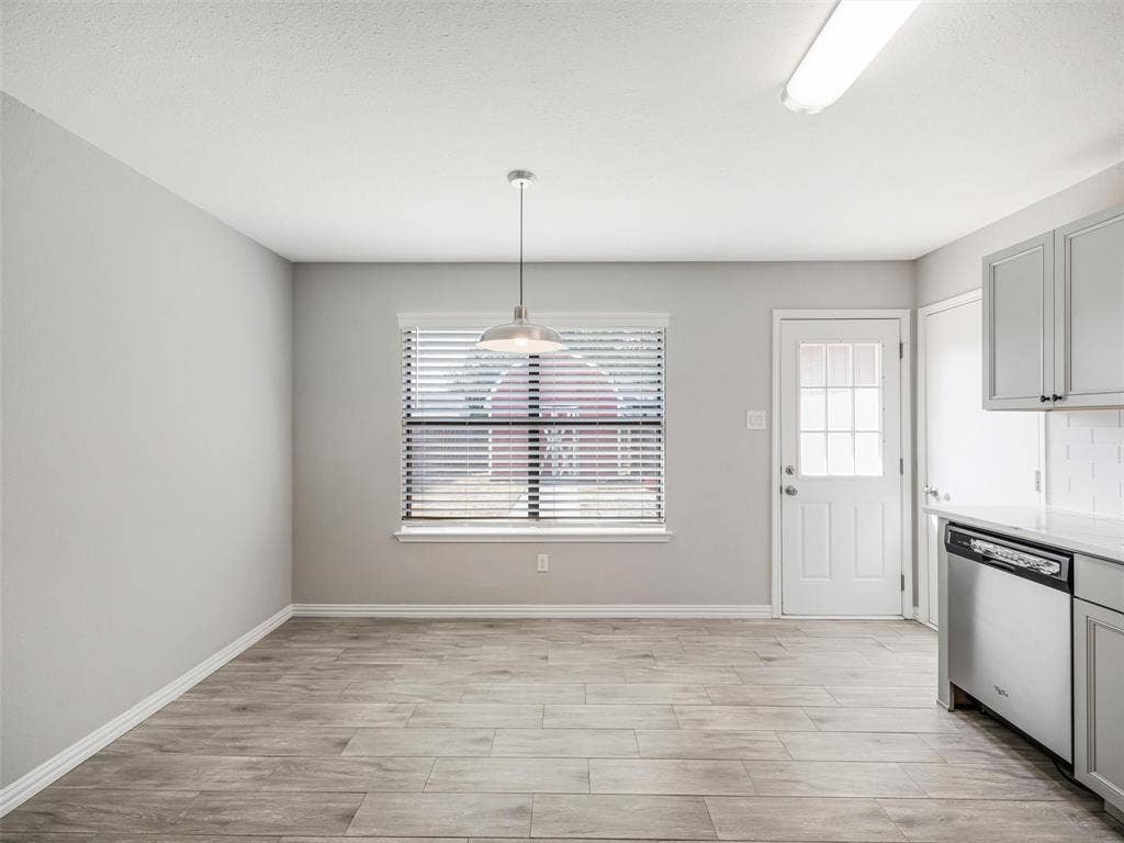 Wood-finish flooring, a window with blinds, a pendant light fixture, a paneled door with glass inserts, and gray cabinetry