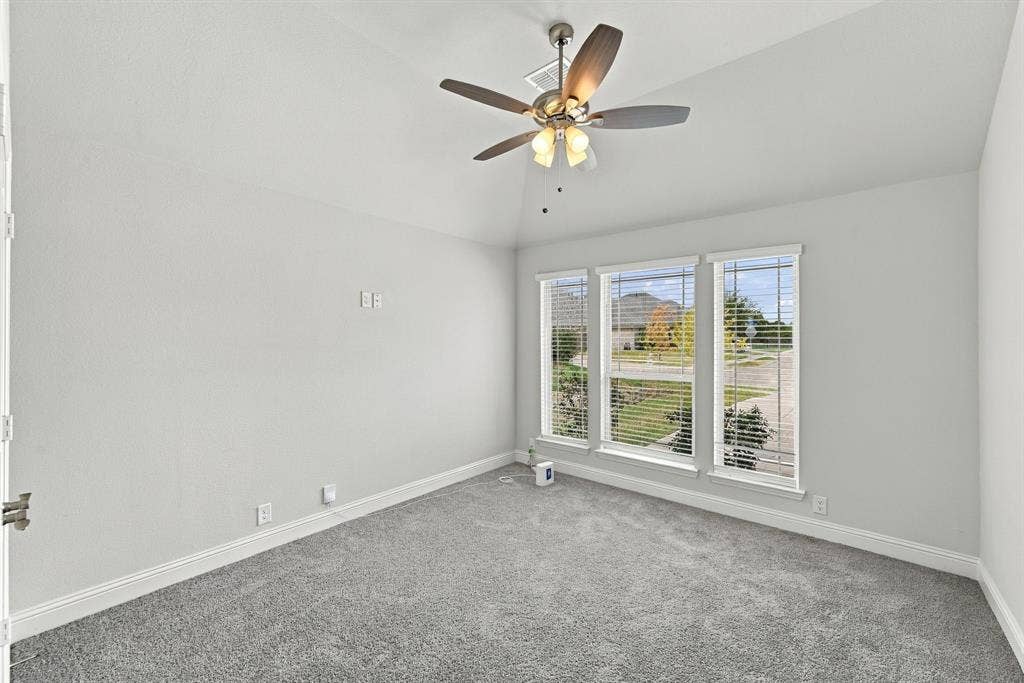 Vaulted ceiling with a ceiling fan, three large windows, carpeted flooring, and light-colored walls