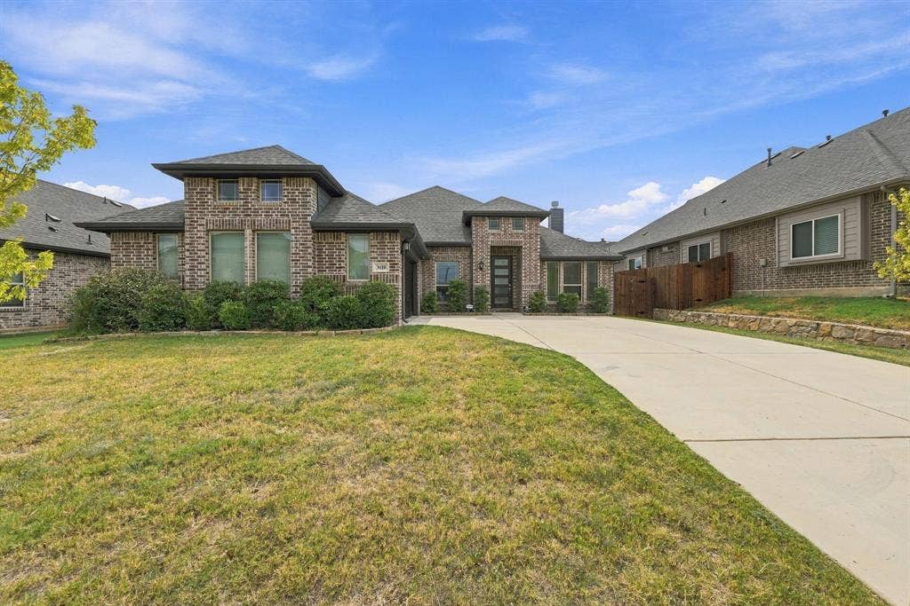 Brick exterior with a prominent entry, an attached garage, a concrete driveway, and a fenced side yard